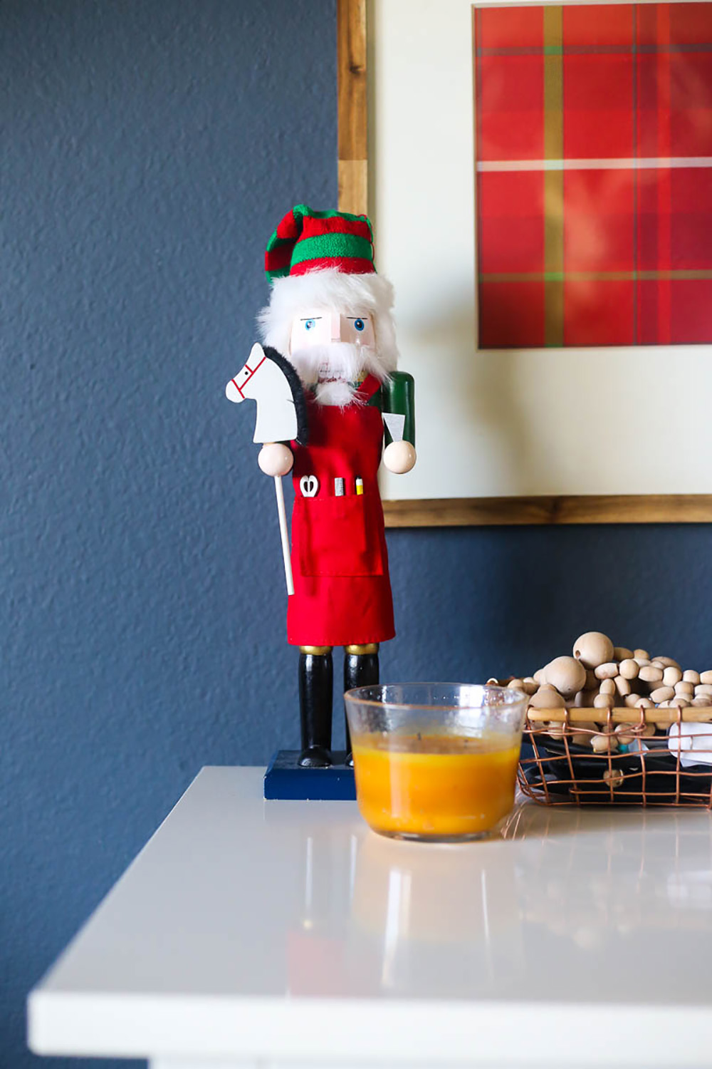 A nutcracker sitting on a white dresser in front of a candle.