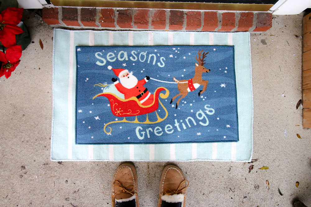 A seasons greetings doormat sits on top of a blue and white rug. A seasons greetings doormat sits on top of a blue and white rug.