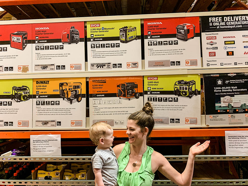 A woman holding a child stands in front of a shelf of generators.