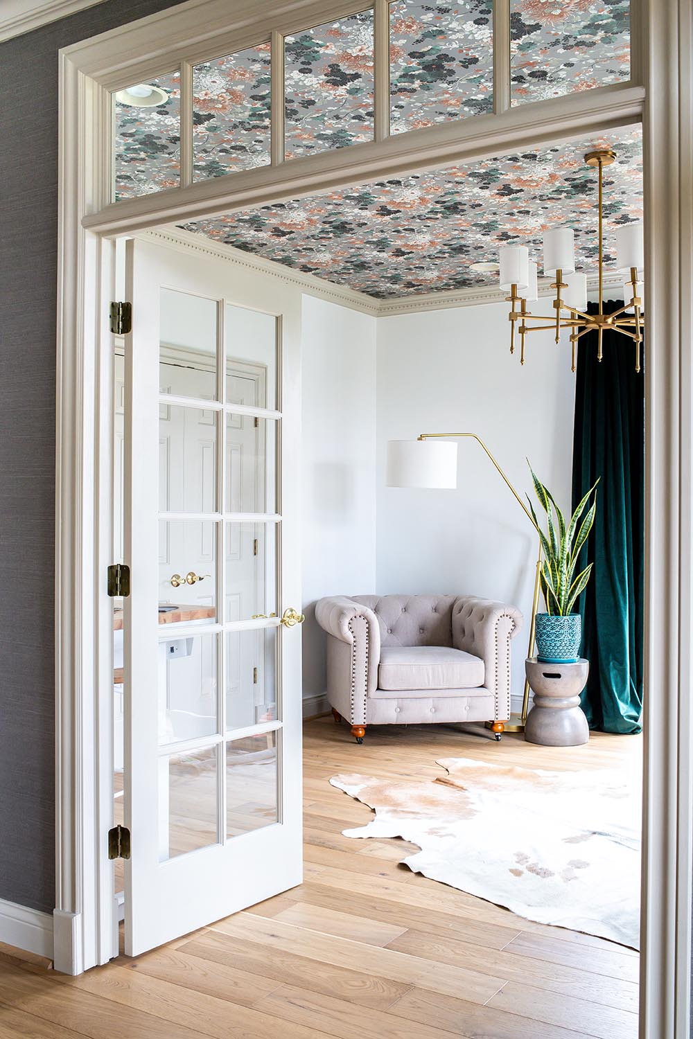 The after of a home office with bright walls, a floral wallpaper ceiling, and brass chandelier.