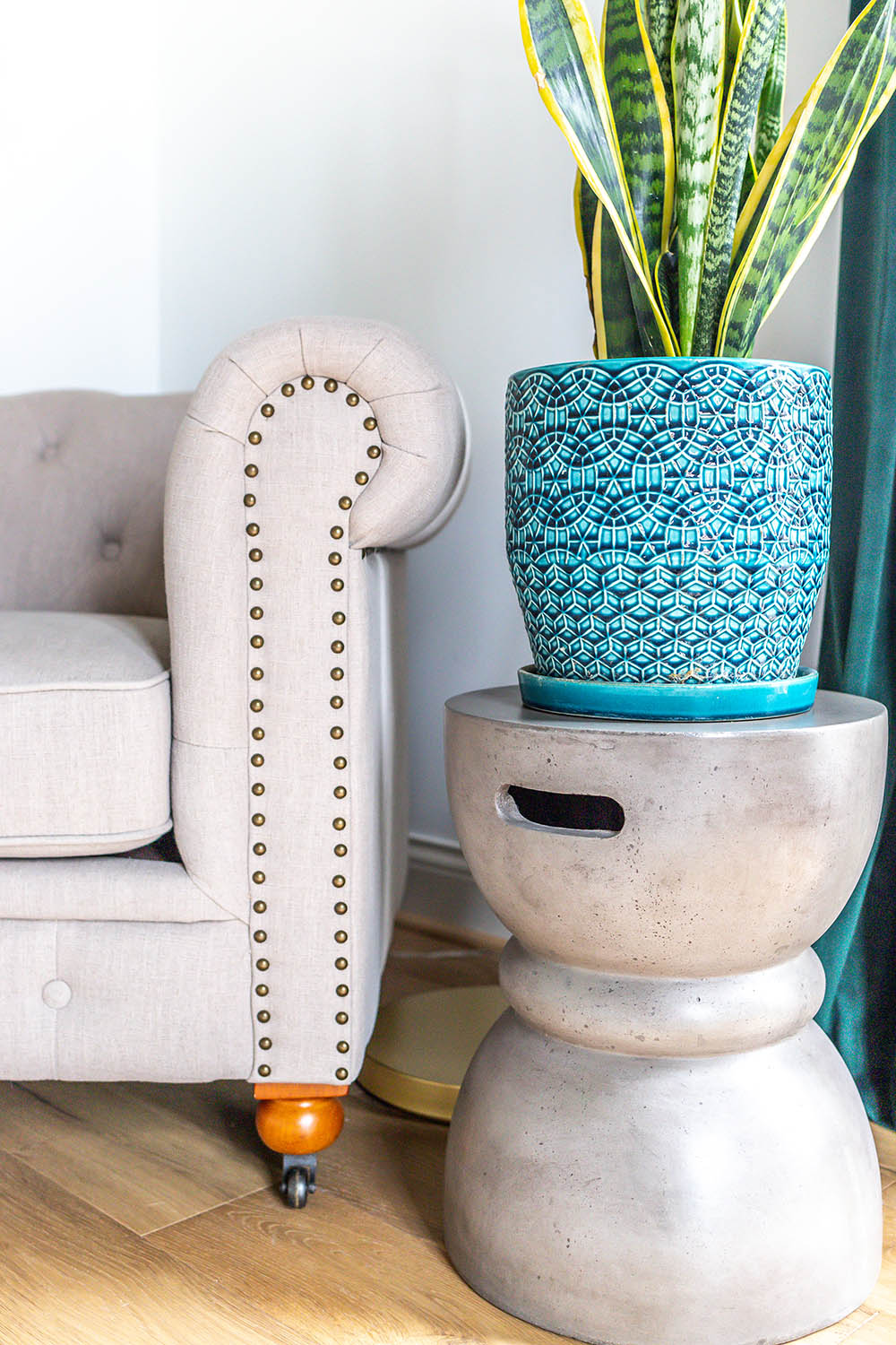 A snake plant in a turquoise and blue planter sits on top of a concrete accent table.