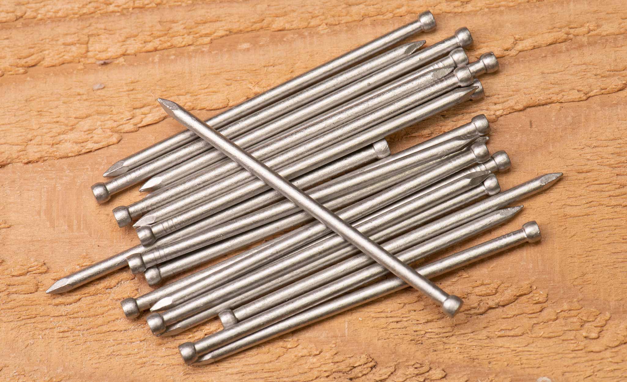 Hot galvanized roofing nails scattered on a cork board.