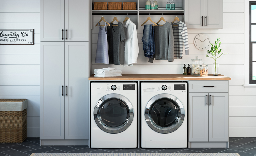 Cabinets, shelves and space for hanging clothes surround a washer and dryer in an organized laundry room.