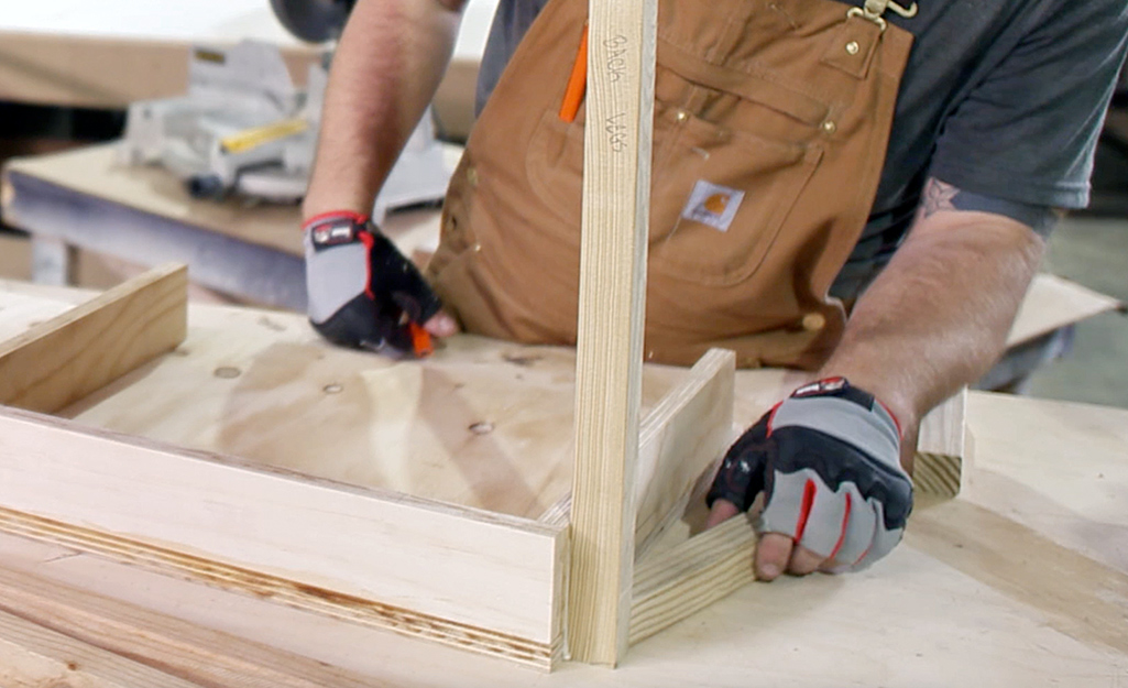 A person begins attaching legs to the wooden box of a DIY desk, which has been placed upside down.