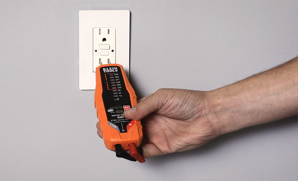 A person using a volt tester on an electrical outlet.