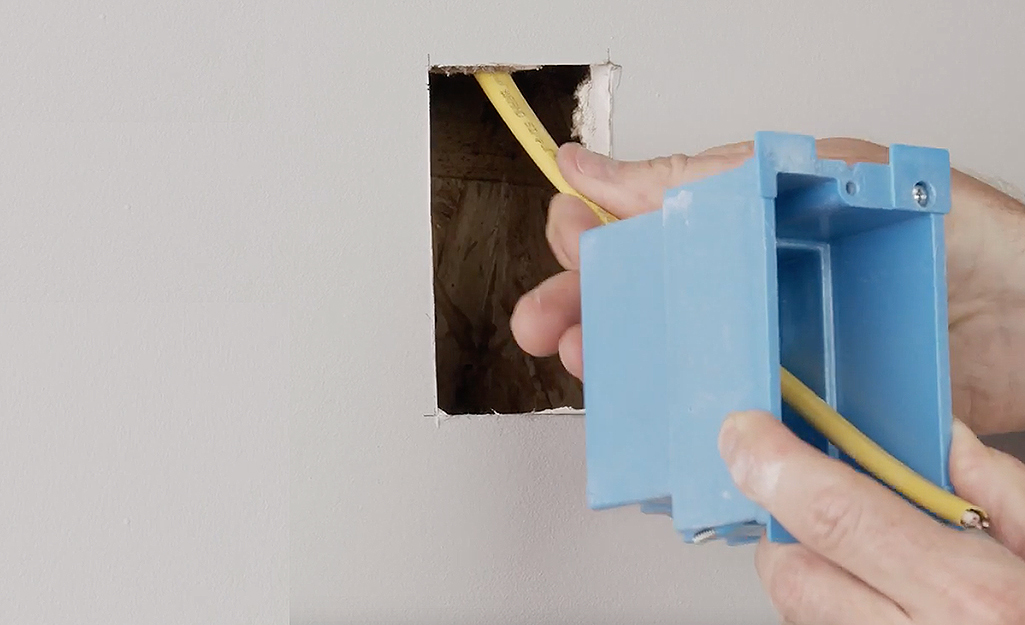 A person running yellow electrical cable into a new switchbox.