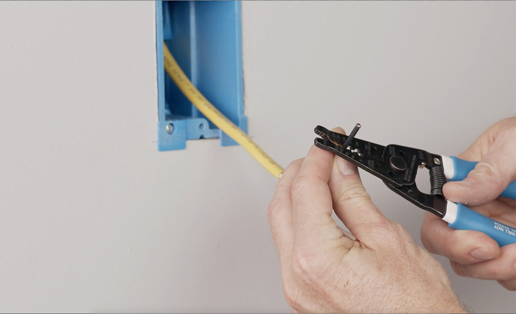 A person stripping the wire on a yellow electrical wall cable.