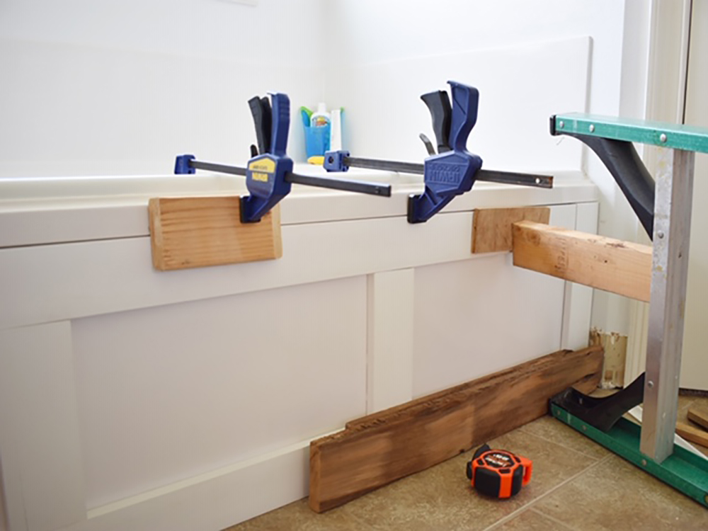 Pieces of moulding are secured to the side of a bathtub with clamps.