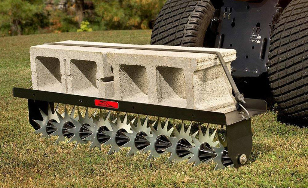 A lawn aerator, weighed down by cement blocks, being pulled behind a garden tractor.