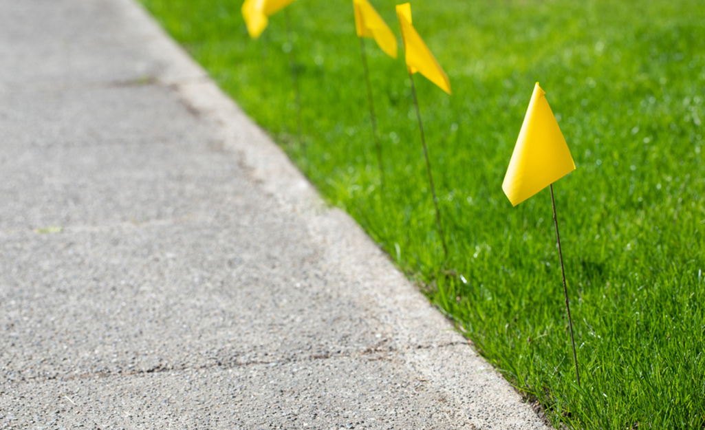 Yellow irrigation flags marking the edge of a walkway in a green lawn.