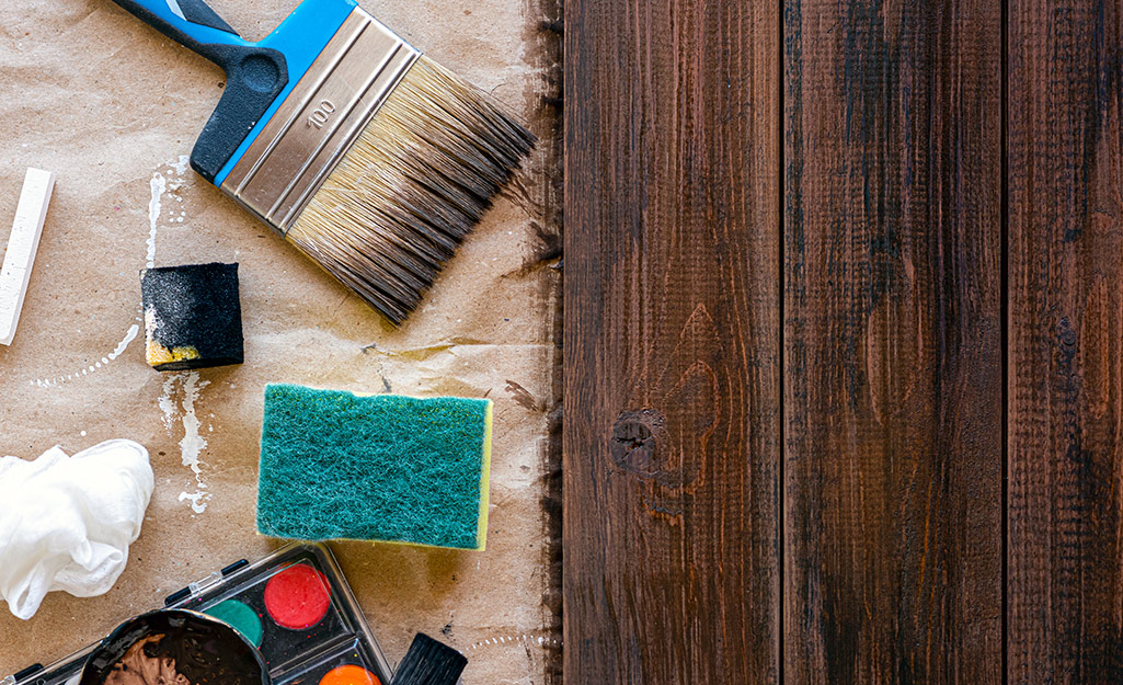 A paint brush and other tools placed next to a freshly stained wood board.