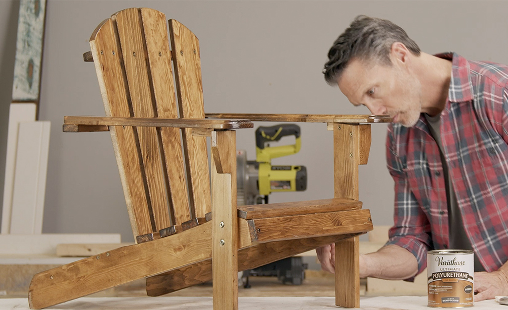 A man adding a final coat of polyurethane to a wood chair.