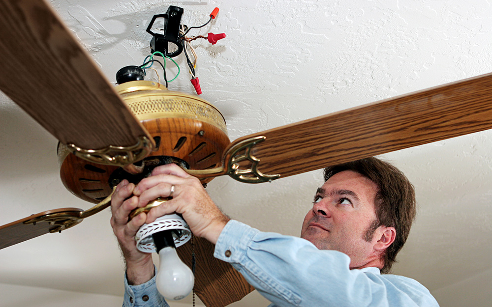 A man removing a ceiling fan to check the blades.