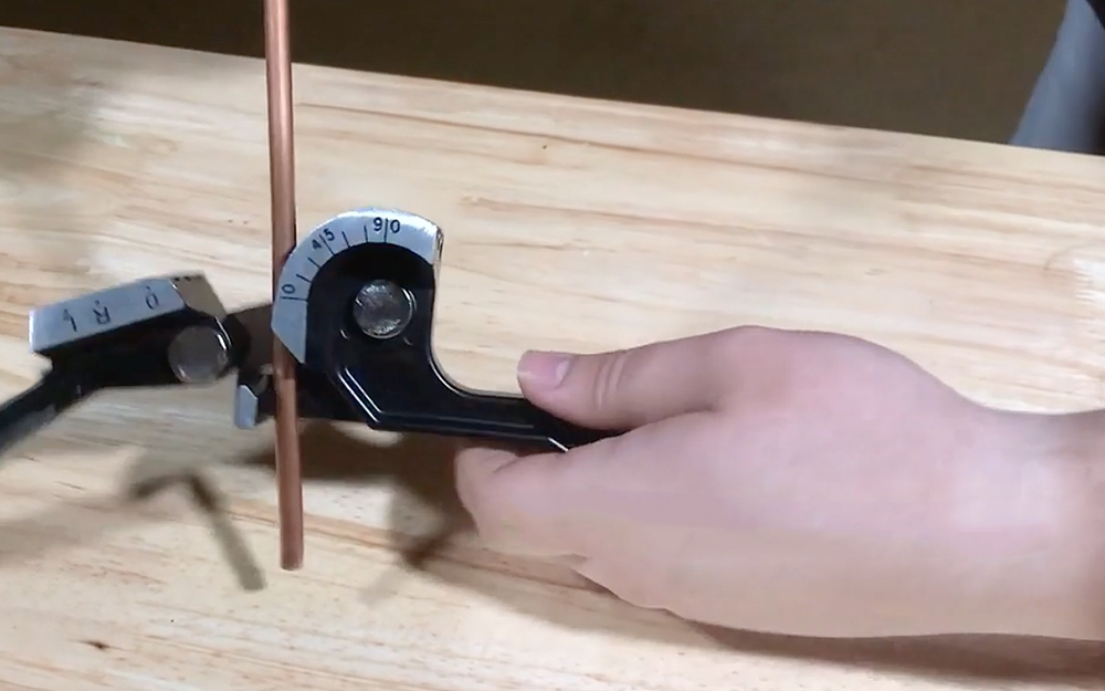 A person places copper tubing in a manual bender.