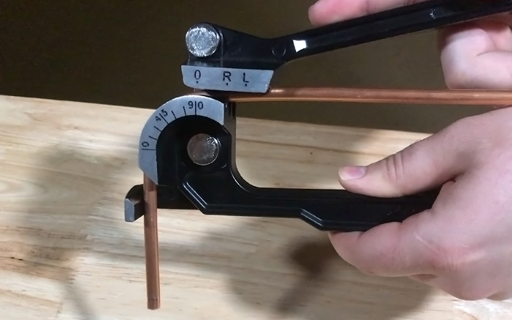 A person bends copper tubing in a manual bender.