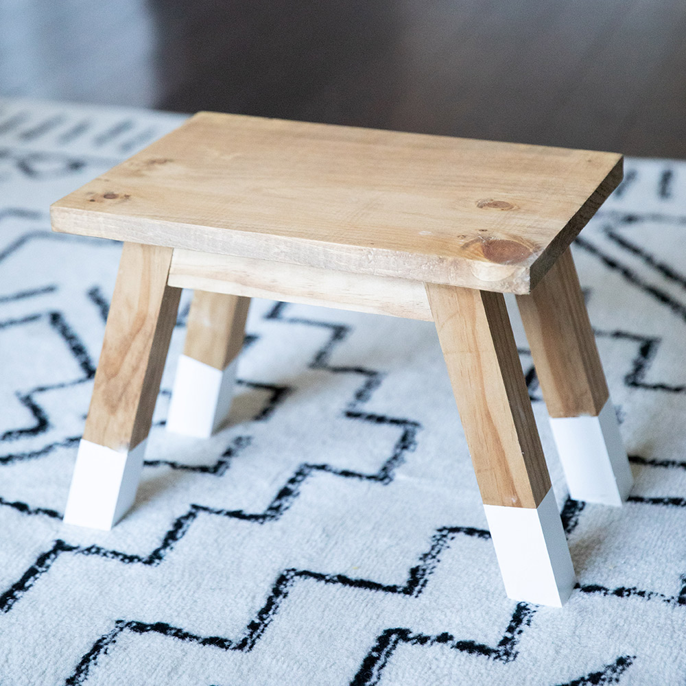 A wooden stool on top of a rug.