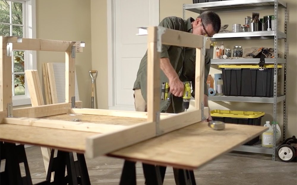 A person drilling the frame of a workbench.