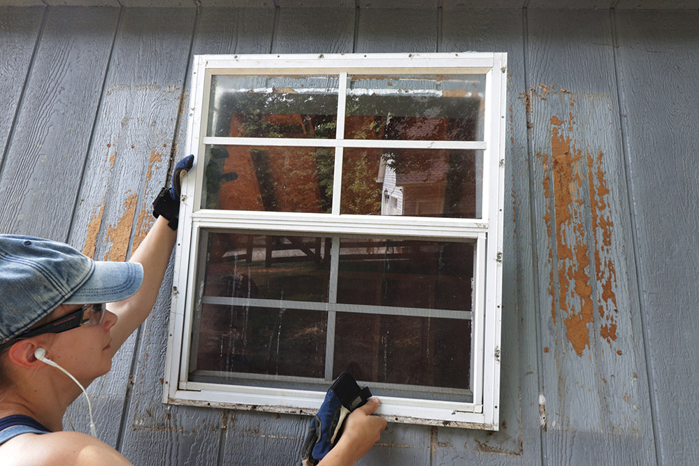 A person removing a window outside of a barn 