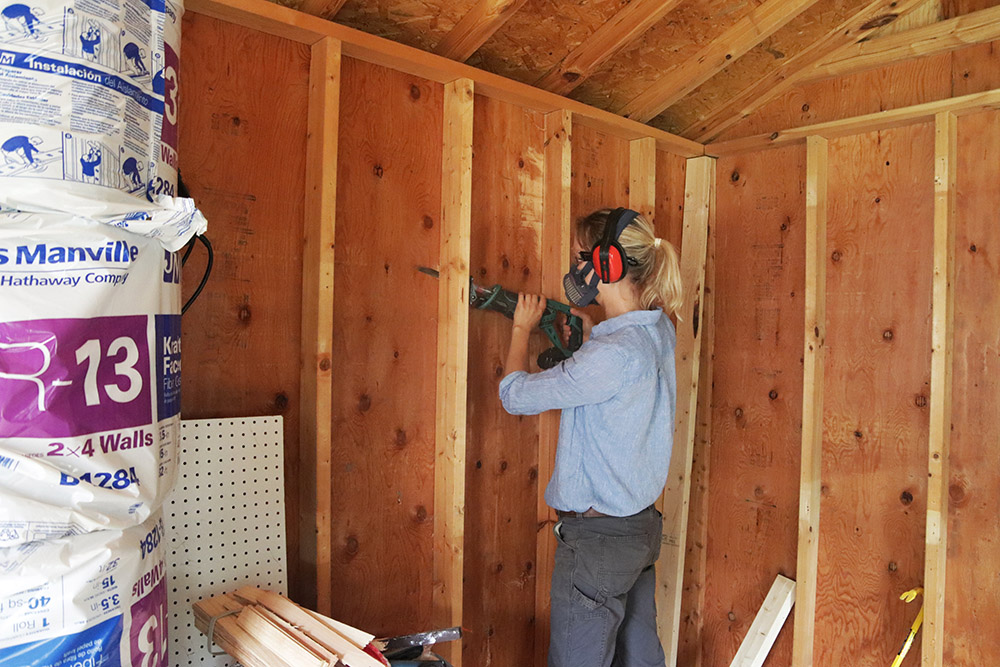 A person cutting a wood wall in a barn 