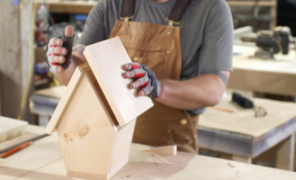 A person piecing together the top of the birdhouse.