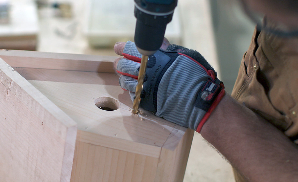 A person drills a hole for a birdhouse perch.