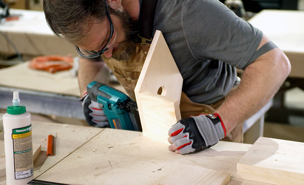 A person uses a drill on the front of the birdhouse.