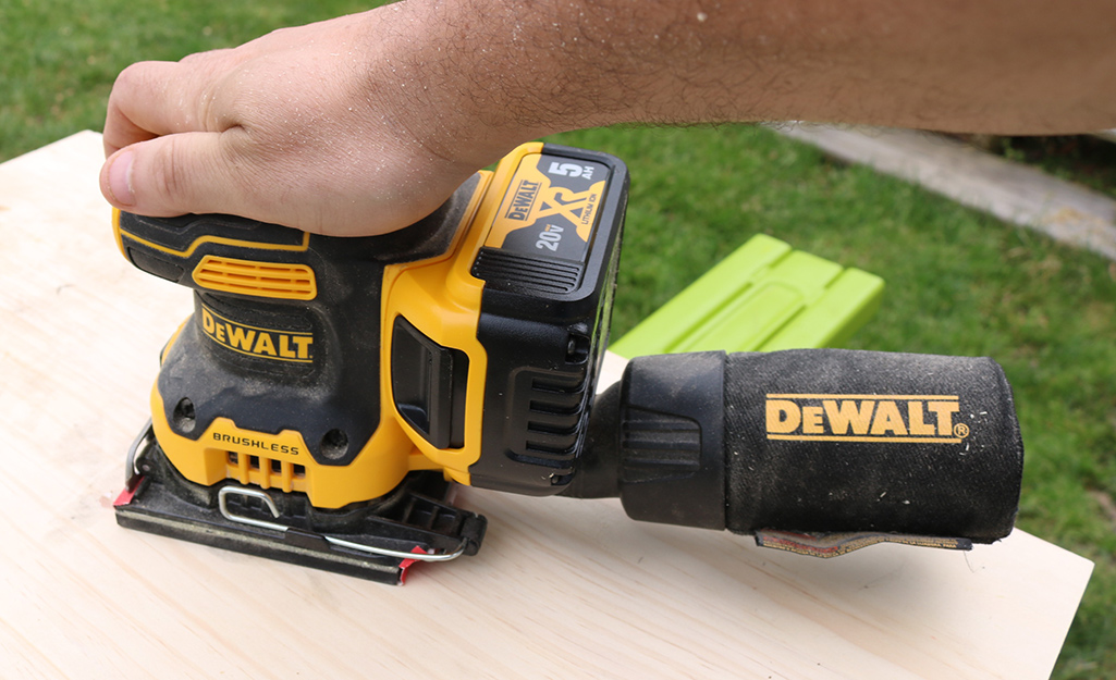 Someone using a cordless sheet sander to sand a board.