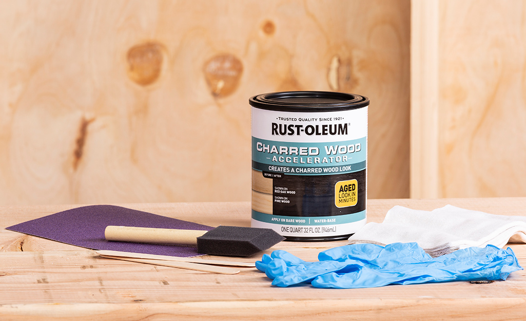 A can of wood stain and wood staining supplies sit on a piece of wood.