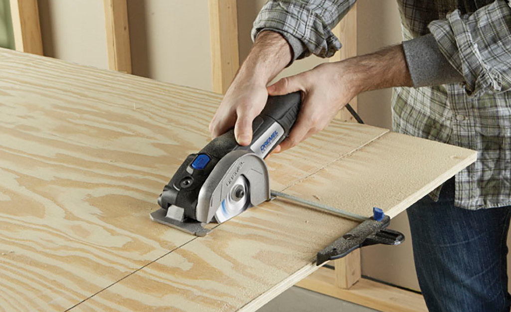 A man uses a handheld circular saw to cut a board.