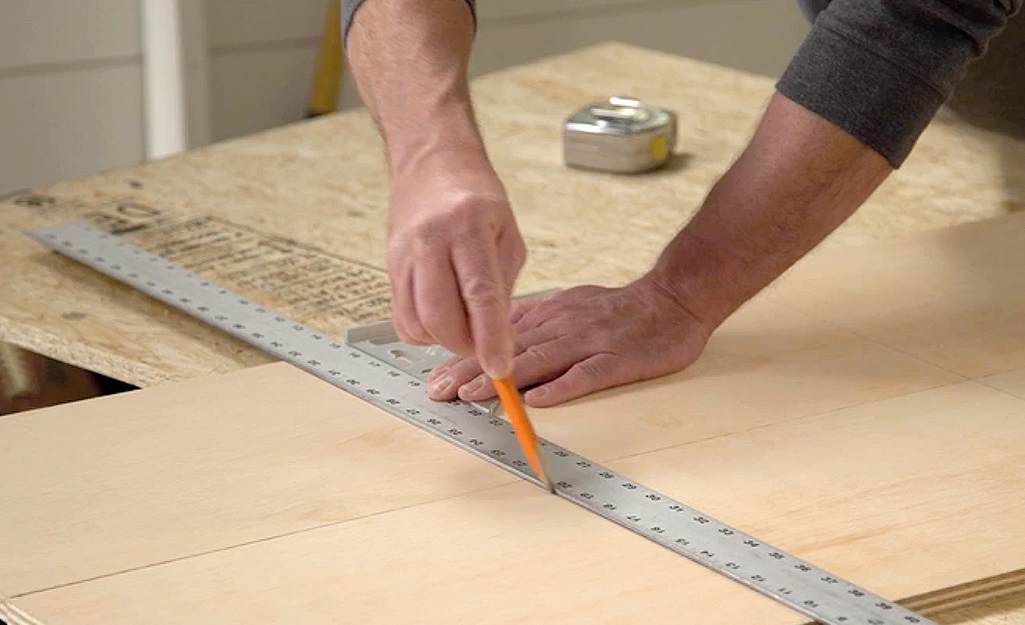 Someone marking a board with a pencil along a metal ruler.