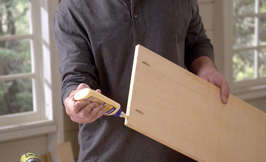 A man squeezing wood glue onto the edge of a board.