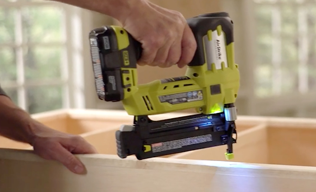 Someone using a nail gun to fasten the face frame of a bookshelf.