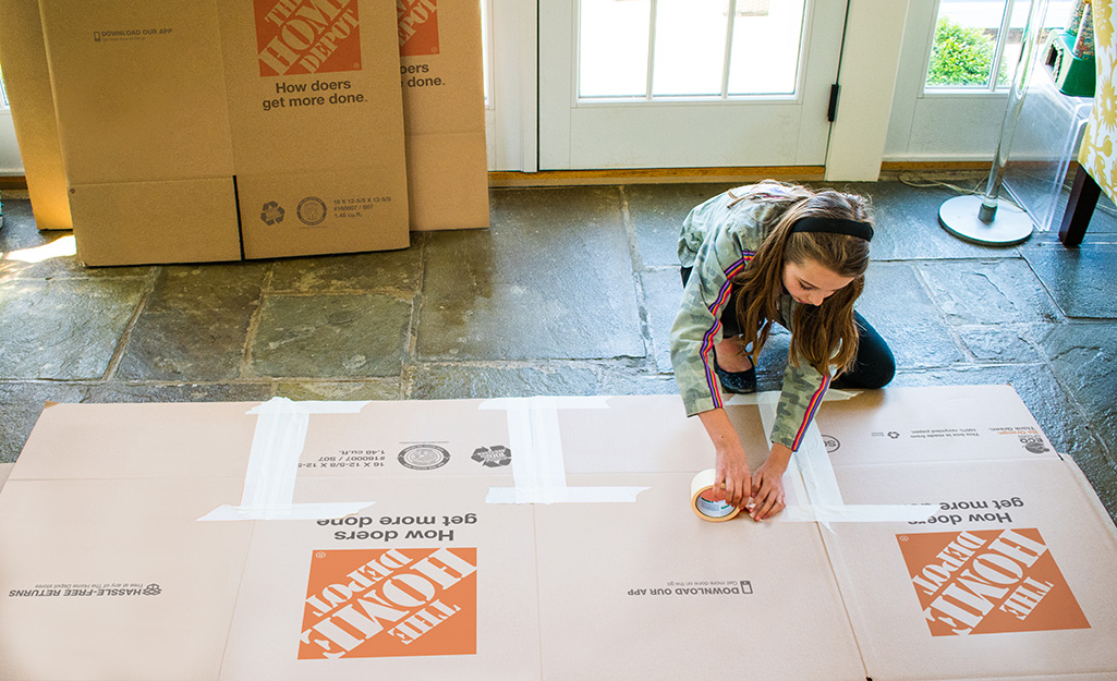 A person taping the seams of cardboard for a deluxe playhouse.