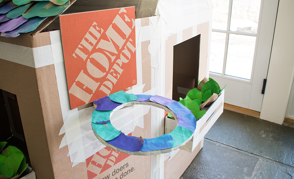 A decorated cardboard basketball hoop attached to a deluxe cardboard playhouse.