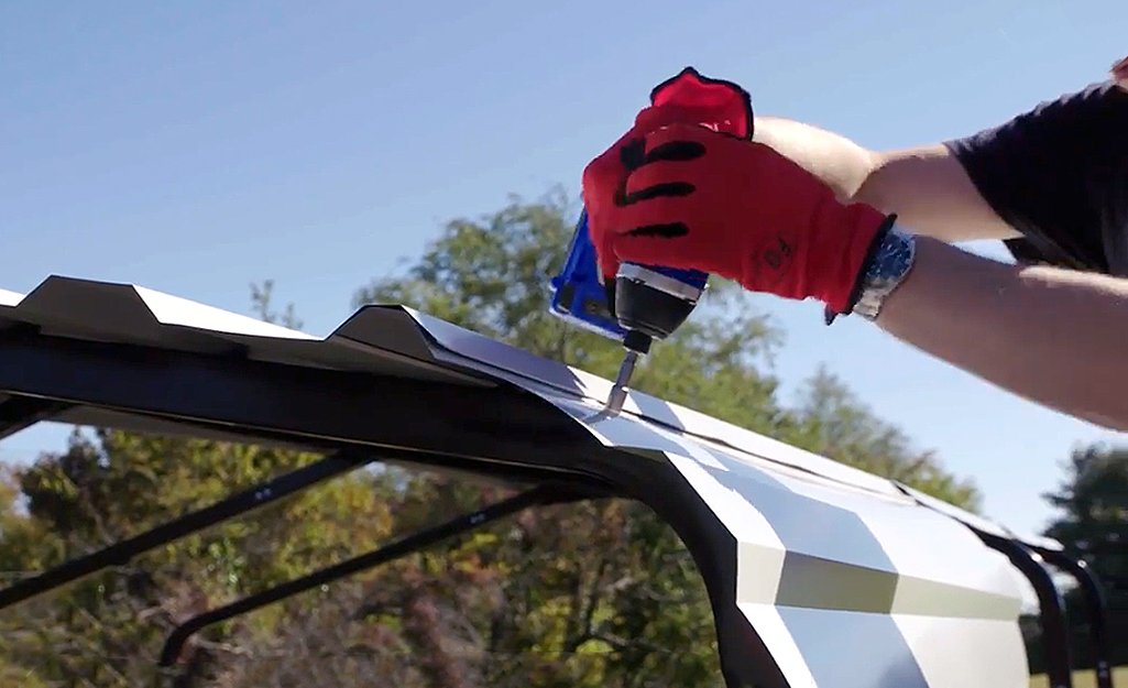 A person use a power drill to attach the roof panels to a metal carport. A person use a power drill to attach the roof panels to a metal carport.