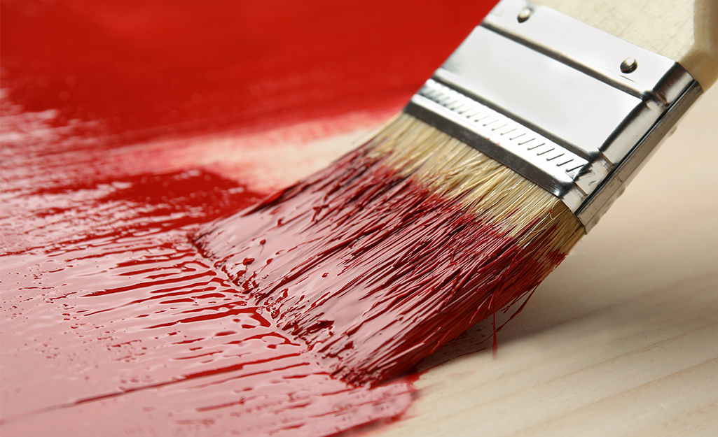 A person brushing red paint over a wood panel.