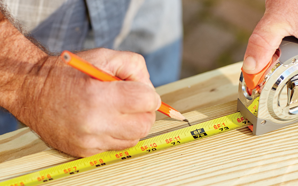 A person marking off measurements on a piece of wood A person marking off measurements on a piece of wood