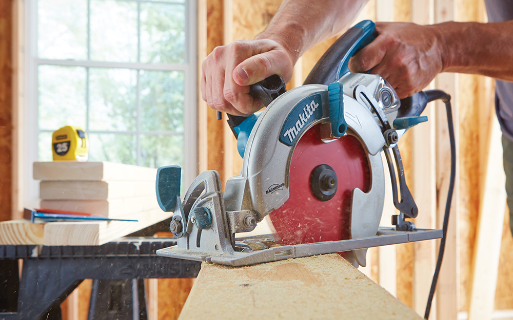 A person cutting a piece of wood with a red-blade circular saw. A person cutting a piece of wood with a red-blade circular saw.