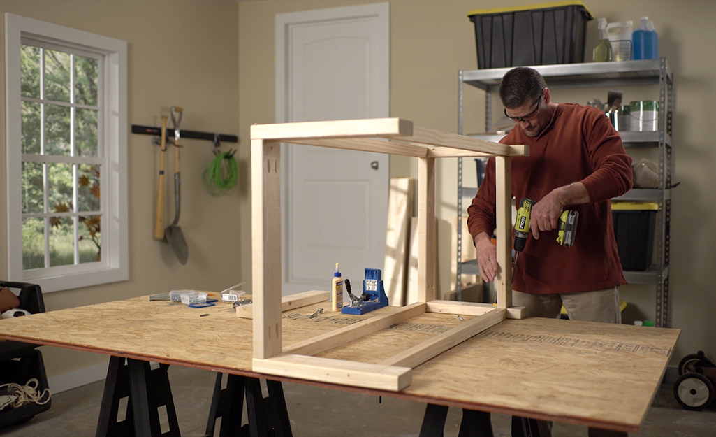 A man using a drill to assemble a DIY coffee table.