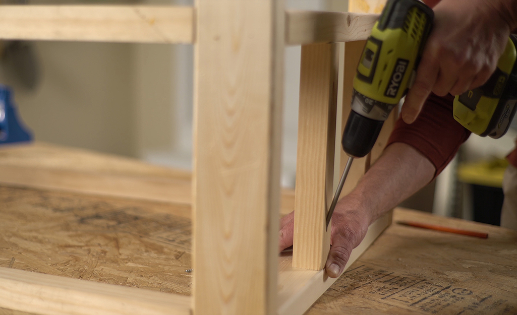 A  man using a drill to make pocket holes in the legs of a DIY coffee table.