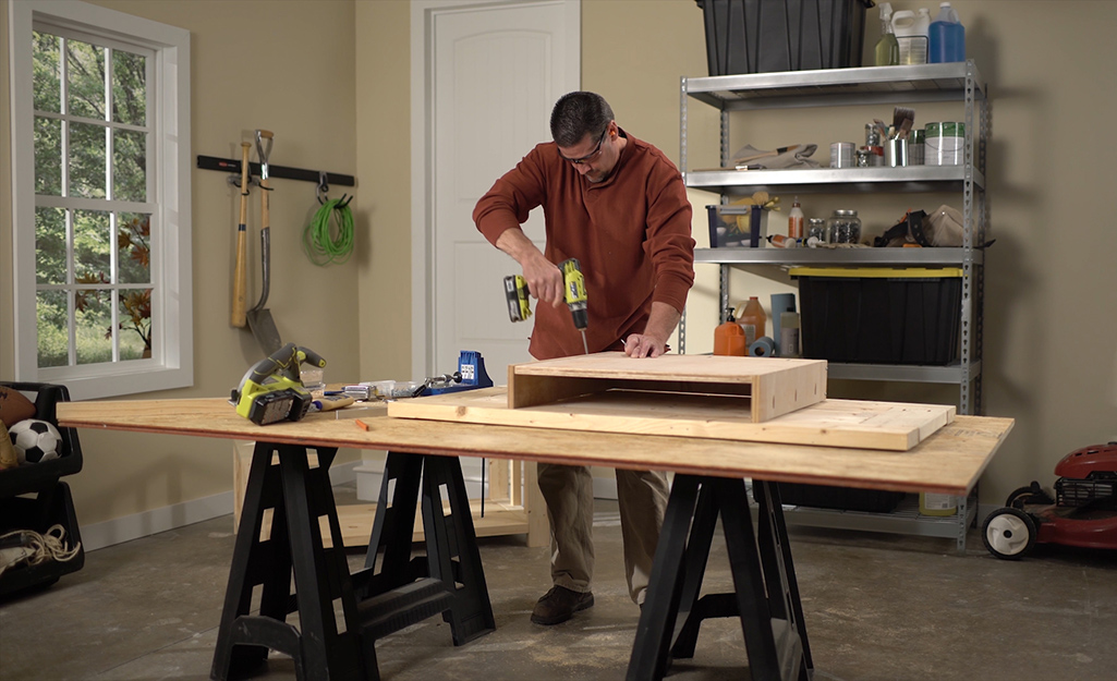 A man using a drill to screw together a shelf for a DIY coffee table. 