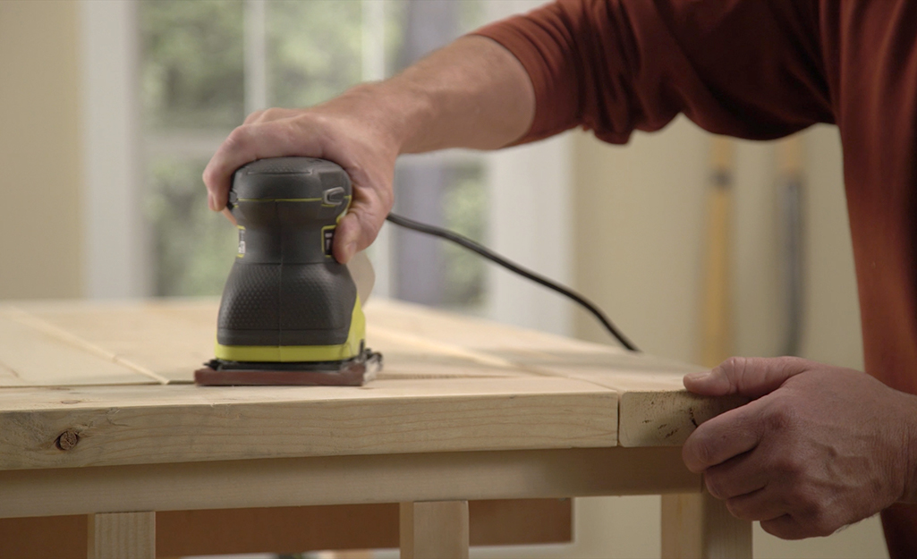 A man using a power sander to sand the top of a DIY coffee table.