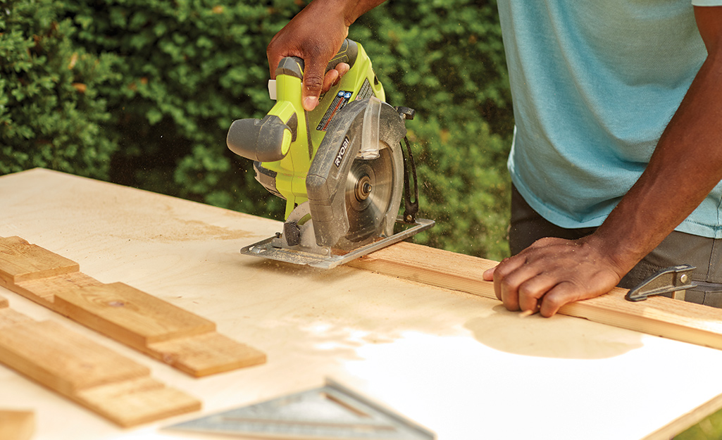 A person uses a circular saw to cut pieces of wood for the top of a cold frame.