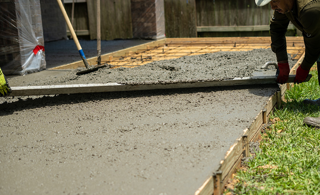 Two people laying a concrete foundation.