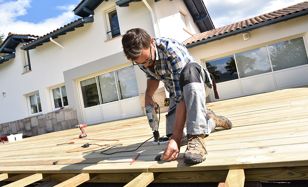 A worker nails boards to the roof of a covered deck.