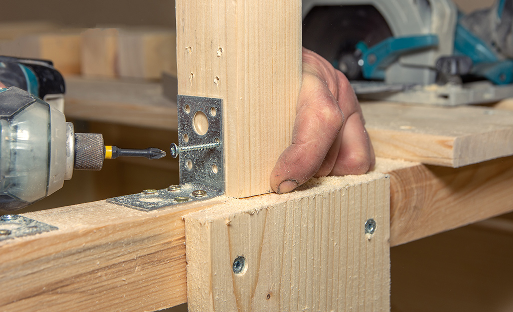 Man attaches a deck board to an inner joist with a power drill.
