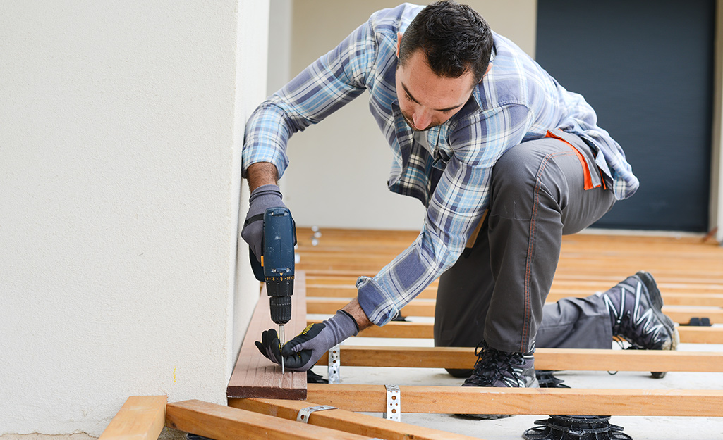 Man attaches a deck board to an inner joist with a power drill. Man attaches a deck board to an inner joist with a power drill.