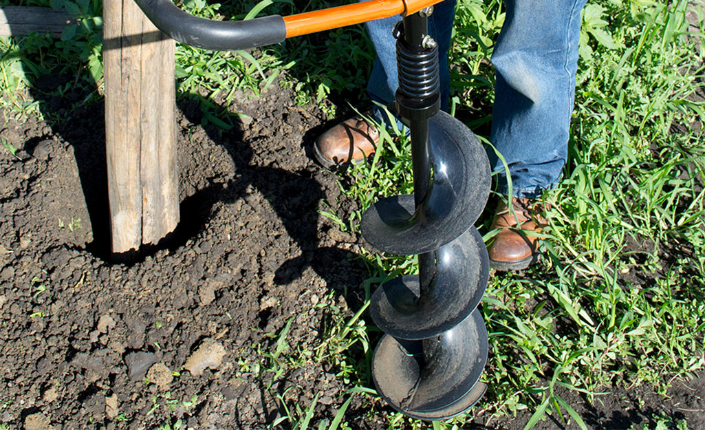 Man uses an auger to dig a post hole. Man uses an auger to dig a post hole.