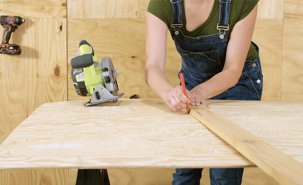 A worker draws lines on plywood for a dog house wall.