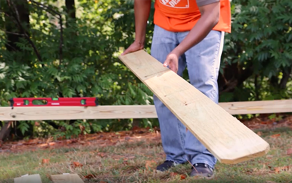 A person moves a board while planning a fence.